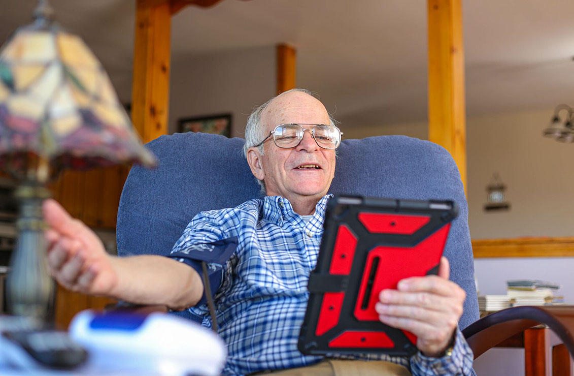 elderly man sitting in a chair and looking at an iPad