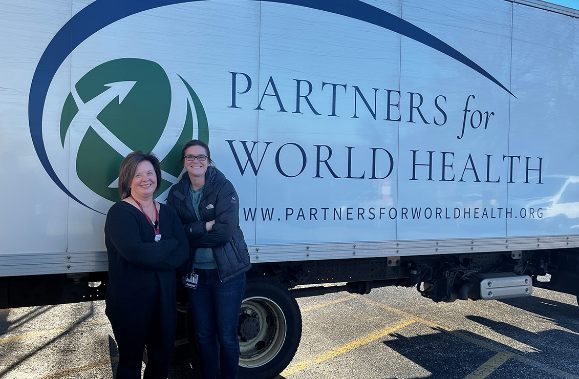 Two women standing next to semi truck with printing on side: Partners for World Health